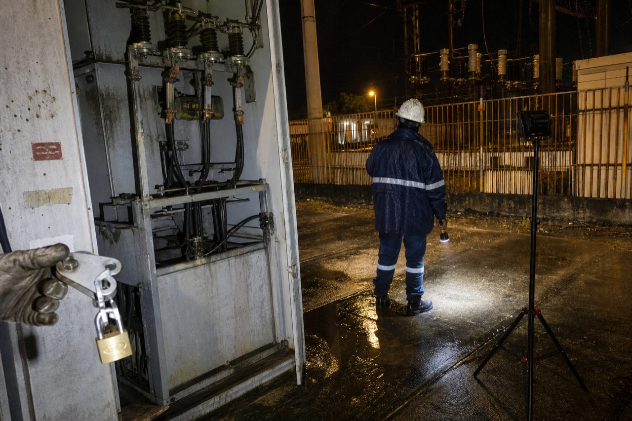 Cabine de média tensão aberta à noite em subestação industrial, com holofote de campo e equipe em atendimento emergencial