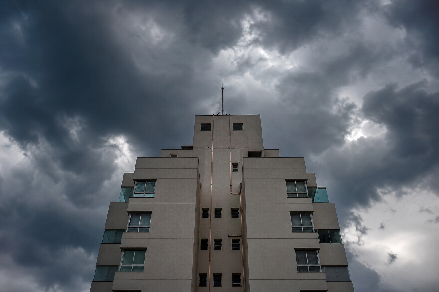 Topo de edifício residencial brasileiro com haste captora Franklin e cabos de descida do SPDA, sob céu de tempestade